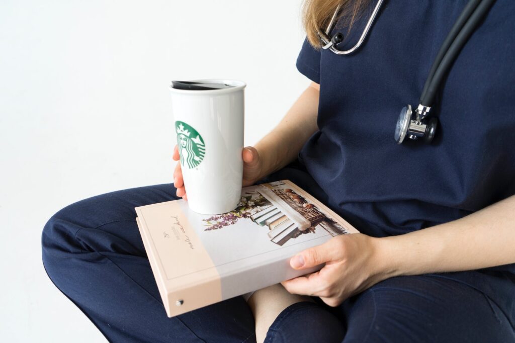 person in blue scrubs holding white and green starbucks cup